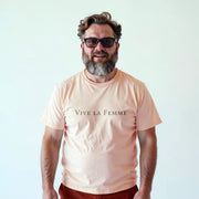 A man with a beard wearing a peach-colored t-shirt with the text 