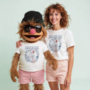 A woman wearing a white t-shirt with a graphic design and a large stuffed animal wearing a black hat and sunglasses standing next to her.