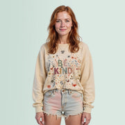 A young woman with red hair wearing a beige sweater with the text 